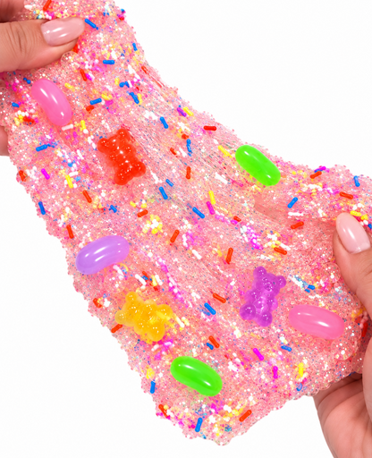 Pink Sugar Rush slime stretched between hands with sugar scrub beads and candy charms